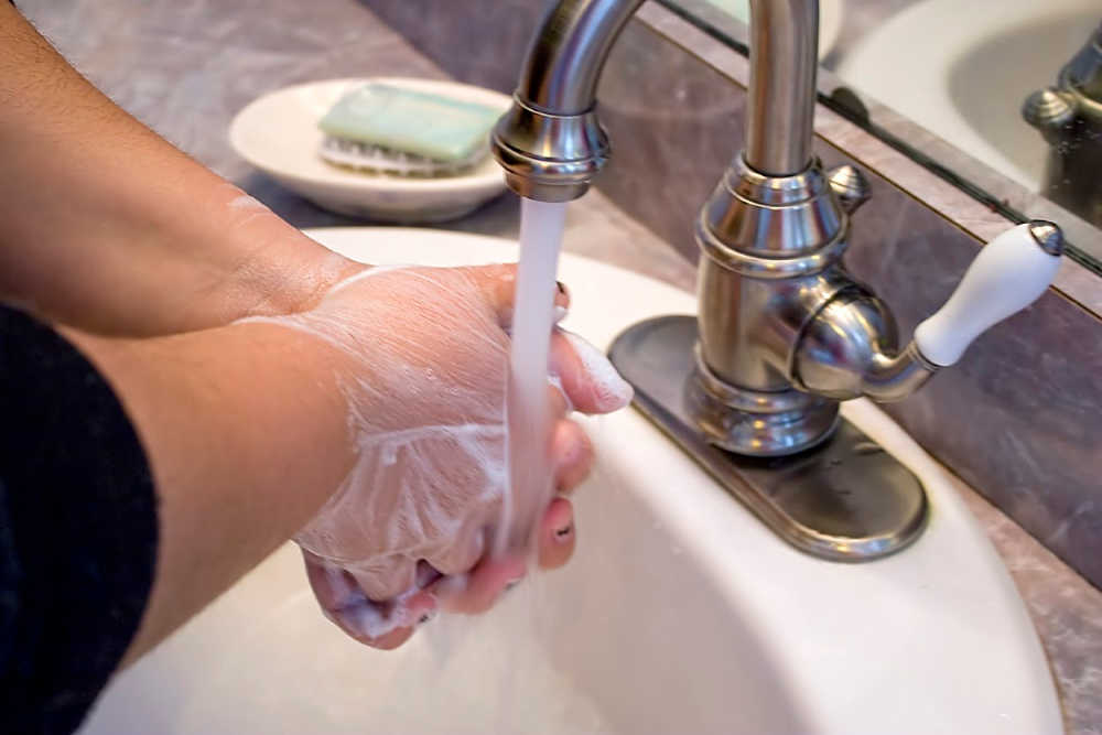 A person washing and rinsing off their hands in the bathroom sink.