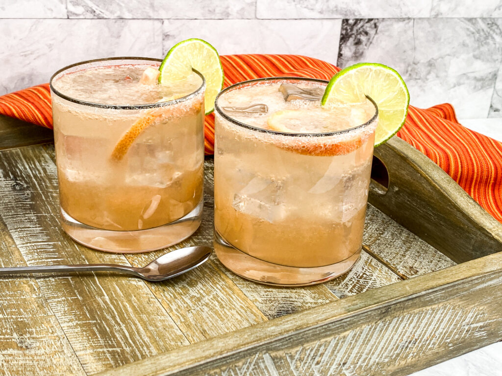 2 whiskey glasses with sparkling Paloma cocktails garnished with lime slices.