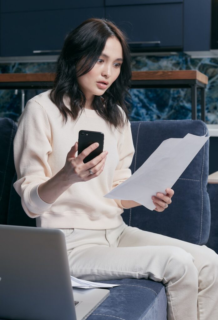 Woman looks stressed out while reading papers and holding a phone.
